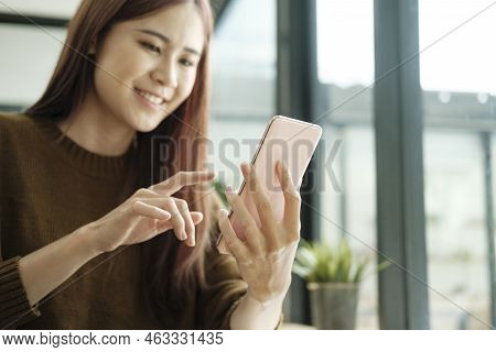 Young Asian Female Student Studying Online Using Laptop And Holding Mobile Phone Surfing The Interne