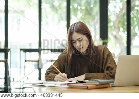 Young Asian Female Student Studying Online Using Laptop And Holding Mobile Phone Surfing The Interne