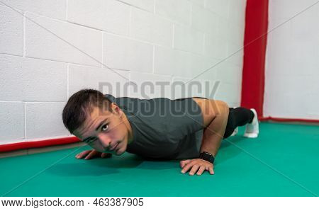 Determined Strong Young Man Doing Push-ups And Looking At Camera. He Is Dressed In An Grey Shirt And