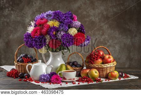 Autumn Still Life. A Vase With Asters, Baskets Of Fruit, Apples And Plums And Porcelain Teaware On T