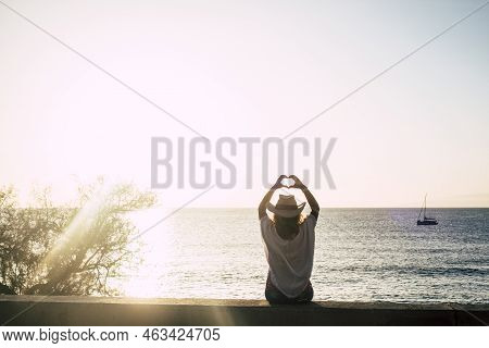 Cute Girl With Cowbly Summer Style Hat Viewed From Back Doing Hearth Sign With Hands - Sun Backlight