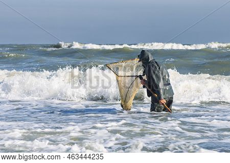Amber Catching In The Baltic Sea. Amber Catcher Or Fisherman With Fisherman\'s Coat And Boots Into T