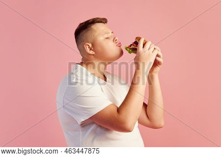Half-length Portrait Of Cute Overweight Boy In White T-shirt Tasting Delicious Burger Isolated On Pi