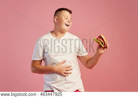 Half-length Portrait Of Cute Overweight Boy In White T-shirt Tasting Delicious Burger Isolated On Pi
