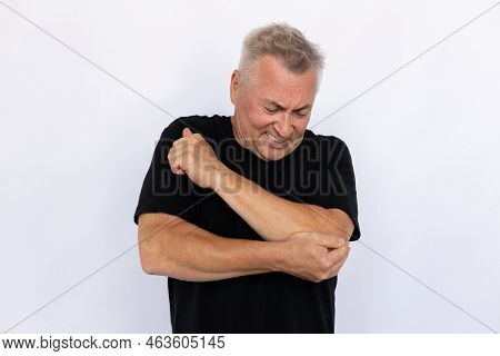 Senior Man Holding Elbow. Male Model In Black T-shirt Experiencing Pain In Elbow With Painful Expres