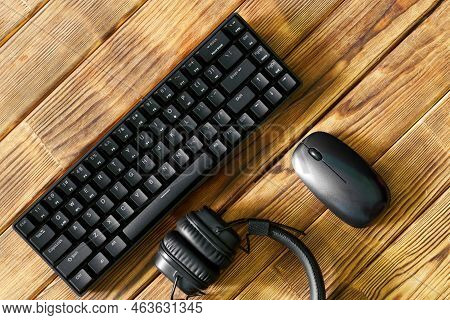 Small Compact Black Computer Keyboard Next To A Computer Mouse And Headphones On A Table Made Of Woo