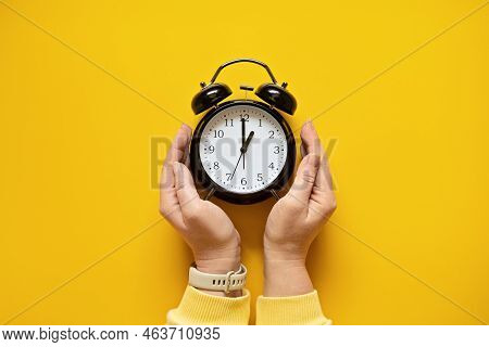 Daylight Saving Day. Fall Back. Black Alarm Clock And Female Hands On Yellow Background. Daylight Sa