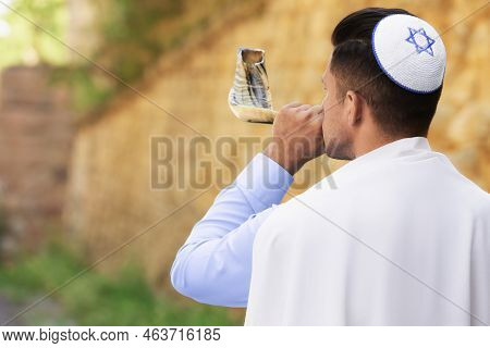 Jewish Man In Kippah And Tallit Blowing Shofar Outdoors. Rosh Hashanah Celebration