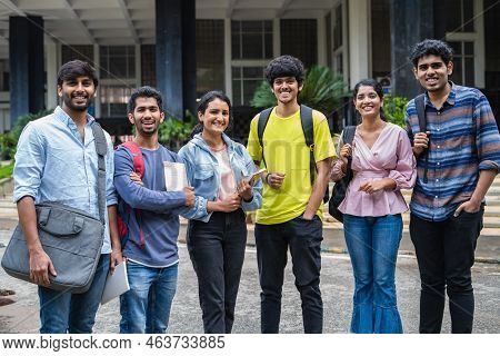 Group Of Happy Students Standing With Books And Backback By Looking Camera At College Campus - Conce