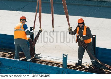 Two Slingers Hook Cargo To Slings In Back Of Truck. Real Workers Unload Cargo. Slingers In Construct