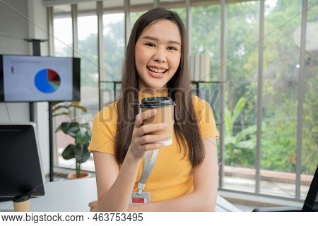 Young Asian Happy Businesswoman Or Intern Holding Coffice Cup In Modern Office Background Is Colleag