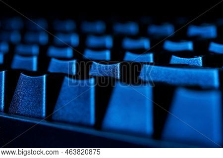 Gaming Computer Keyboard With Black Keycaps Illuminated In The Dark By Blue Light From A Monitor Or 