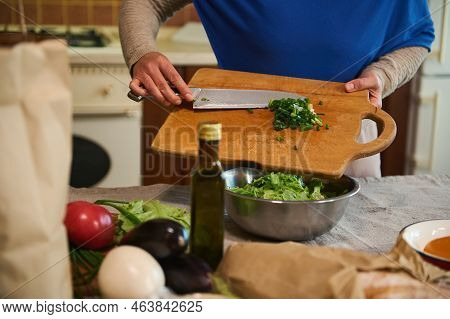 Close-up Of An Unrecognizable Woman Housewife, Pouring Chopped Greens From A Wooden Cutting Board In