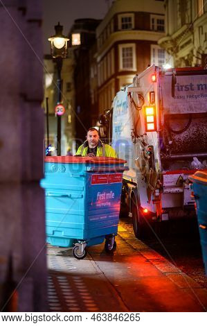 London - November 1, 2020: Bin Man Moves Large Wheelie Bin On Sidewalk At Night