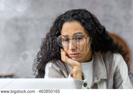 Close-up Photo Of A Sad Woman At Home Reading News Online From A Laptop, A Latin American Woman In T