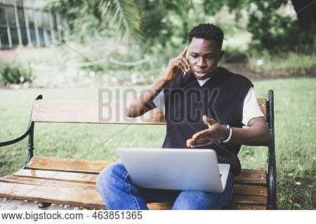 Young African Man Talking On Phone Disputing Over Computer, Stressed, Unsatisfied. Disappointed, Con