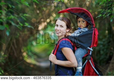 Mother With Toddler Child In Backpack Carrier Is Hiking In Forest. Tourist Is Carrying A Baby On His