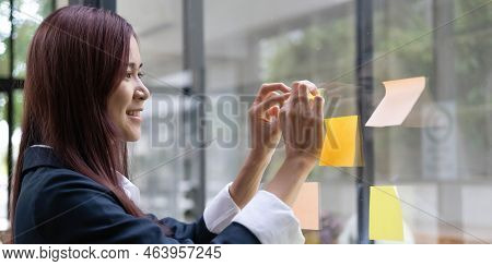 Close-up Of A Woman Hand Holding A Pen Affixing A Note To Her Mirror At The Office.