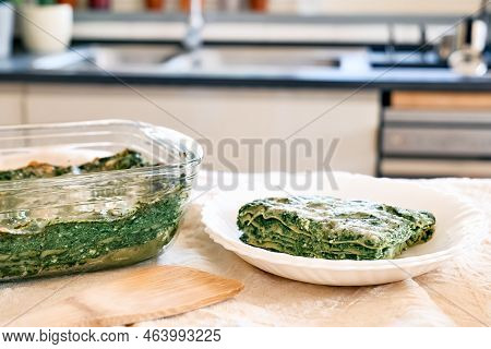 Porzione Of Homemade Lasagna With Spinach And Ricotta In White Plate And In Glass Baking Dish On The