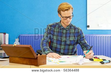 Young cartoonist at work, coloring sketches and drawings behind his desk