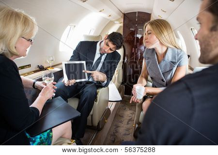 Businessman showing project on digital tablet to partners in private plane
