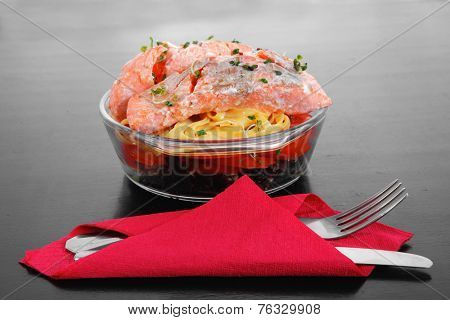 fresh fried natural pink salmon on italian traditional tagliatelles backed with tomato and vegetables served over black wooden table