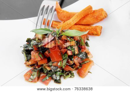 vegetable salad : cherry tomatoes and basil with sweet baked potato served on white plate with sauceboat full blask soy sauce on wood