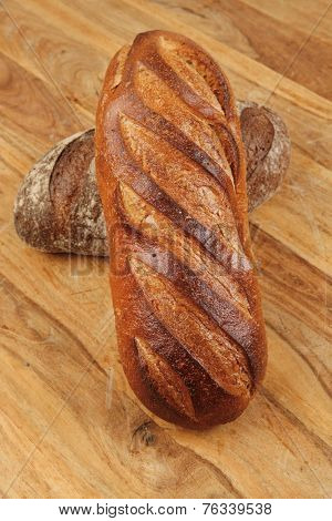 different rye and white flour french bread loaf with on light wooden table background