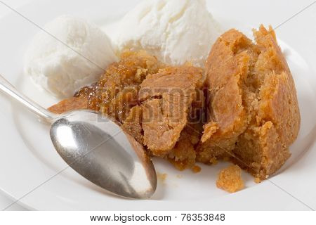 Sussex pond pudding, a steamed British dish filled with a lemon encased in sugar and butter, on a plate with ice cream and a spoon