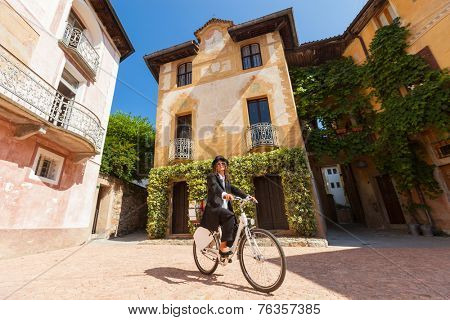 Girl with black elegant dress on a bicycle in the village square