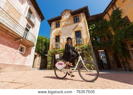 Girl with black elegant dress on a bicycle in the village square