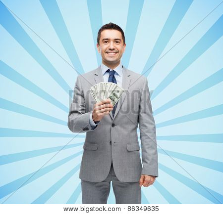 business, people and finances concept - smiling businessman with american dollar money over blue burst rays background