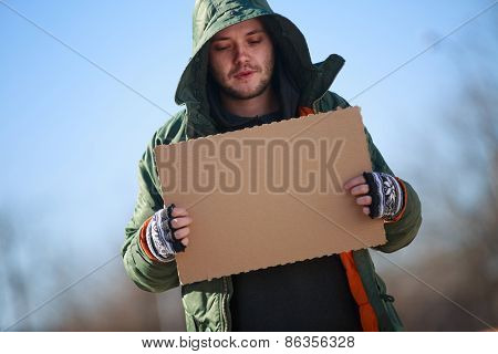 Homeless person with blanck cardboard. Focused on cardboard