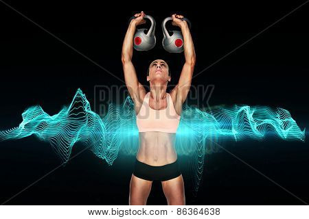 Serious female crossfitter lifting kettlebells above head against blue wave