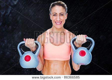 Smiling female crossfitter lifting kettlebells against black background