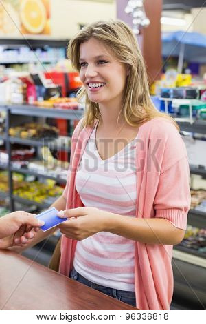 Side view of a smiling woman at cahg register paying with credit card in supermarket