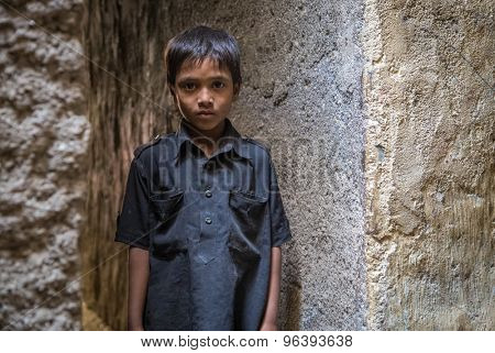 MUMBAI, INDIA - 12 JANUARY 2015: Young Indian boy from Dharavi slum stands in empty narrow street in black shirt.