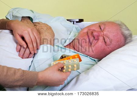 Picture of a sick elderly man with his carer holding medication
