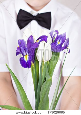 Bouquet of spring flowers in children's hands. Tulips irises - early spring flowers is holding a child. Greetings from the boy in smart clothes. Mother's Day Women's Day a gift a bouquet of flowers.