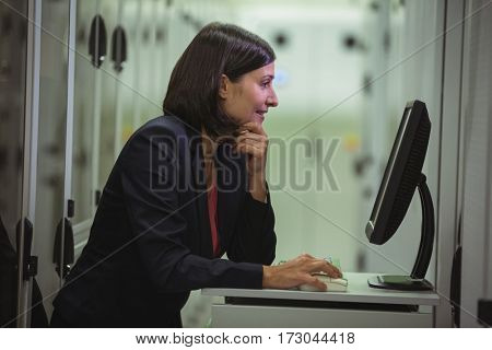 Technician working on personal computer while analyzing server in server room