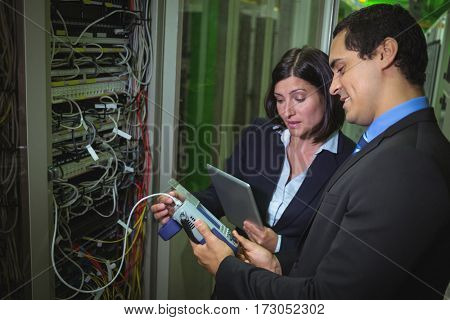 Technicians using digital cable analyzer while analyzing server in server room