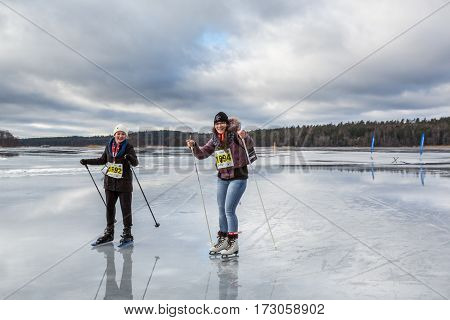Two young woman ice skating together on wet ice.Upplands Vasby, Sweden - February 19, 2017: Two young cheerful woman skating on wet ice late winter day trying to avoid the deep water puddles on the ice. Participants of the annual ice skating event Vikinga