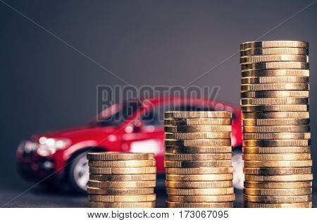Rising piles of coins and a red car in the background