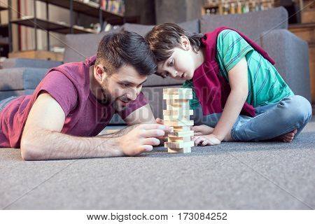 smiling father and focused son playing jenga game at home