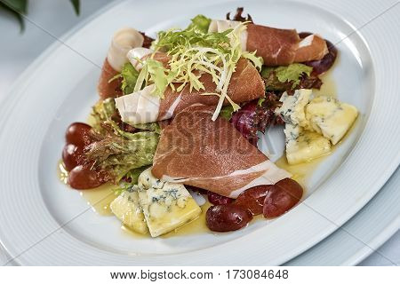meat salad with ham cheese lettuce Dorblu grapes and olive oil served on a plate on a table with flowers