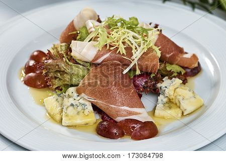 meat salad with ham cheese lettuce Dorblu grapes and olive oil served on a plate on a table with flowers