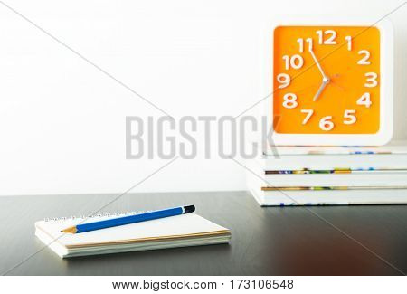 Orange clock on stacked book with white copy space wall for writter