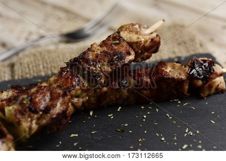 closeup of some barbecued spiced chicken meat skewers on a slate tray, placed on a rustic wooden table