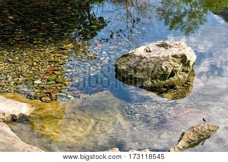 stone in calm water with strong sky reflection