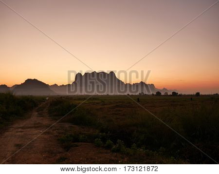 Silhouette of mount zwegabin in Hpa-an Myanmar during morning sunrise with a small path on the left leading into fields close to the mountain